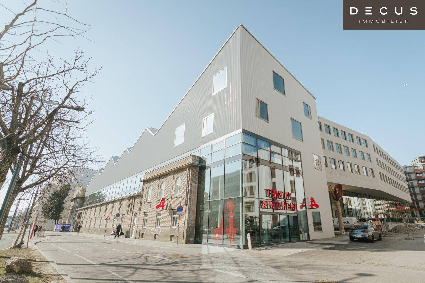 Weitläufiger moderner Gebäudekomplex mit markanter Architektur und Glasfassade an einer städtischen Straße.