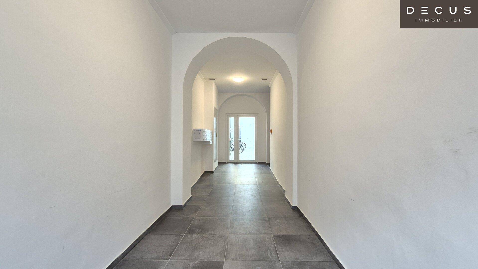 Langer, heller Flur mit modernen Fliesen und einem eleganten Bogendurchgang am Ende.