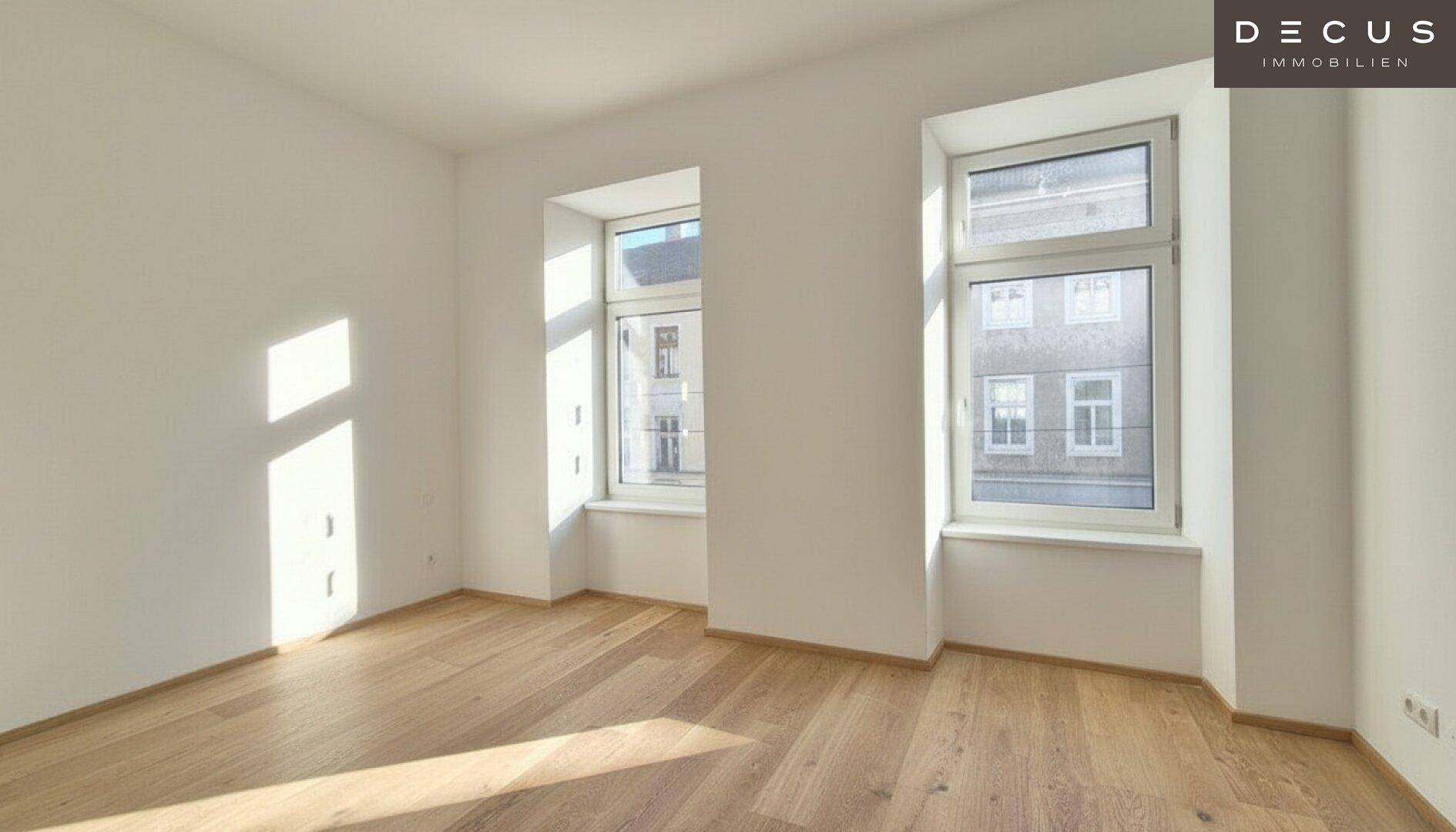 Lichtdurchfluteter Raum mit zwei großen Fenstern und elegantem Holzboden, der eine helle Atmosphäre schafft.