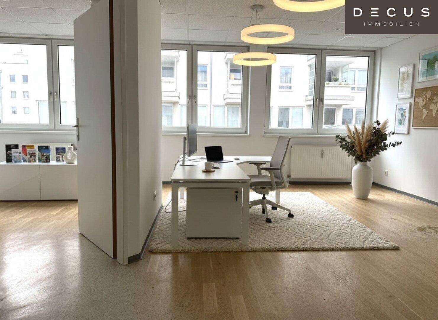 Helles Büro mit Holzboden, modernen Deckenleuchten und Blick auf umliegende Gebäude.