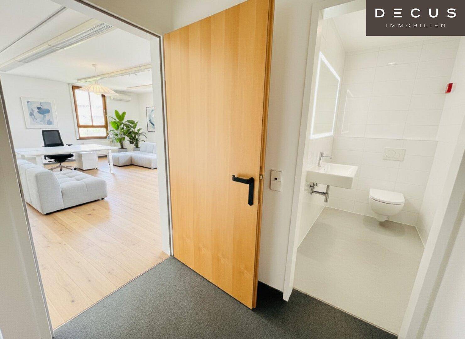 Blick vom Flur in ein modernes Badezimmer mit WC und Waschbecken sowie in einen hellen Bürobereich.
