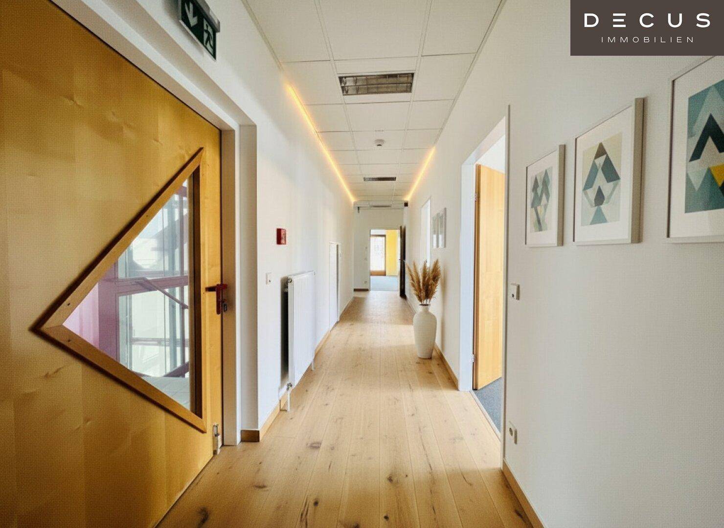 Heller Flur mit Holzboden, modernen Wandbildern und indirekter Beleuchtung, führt zu weiteren Räumen.