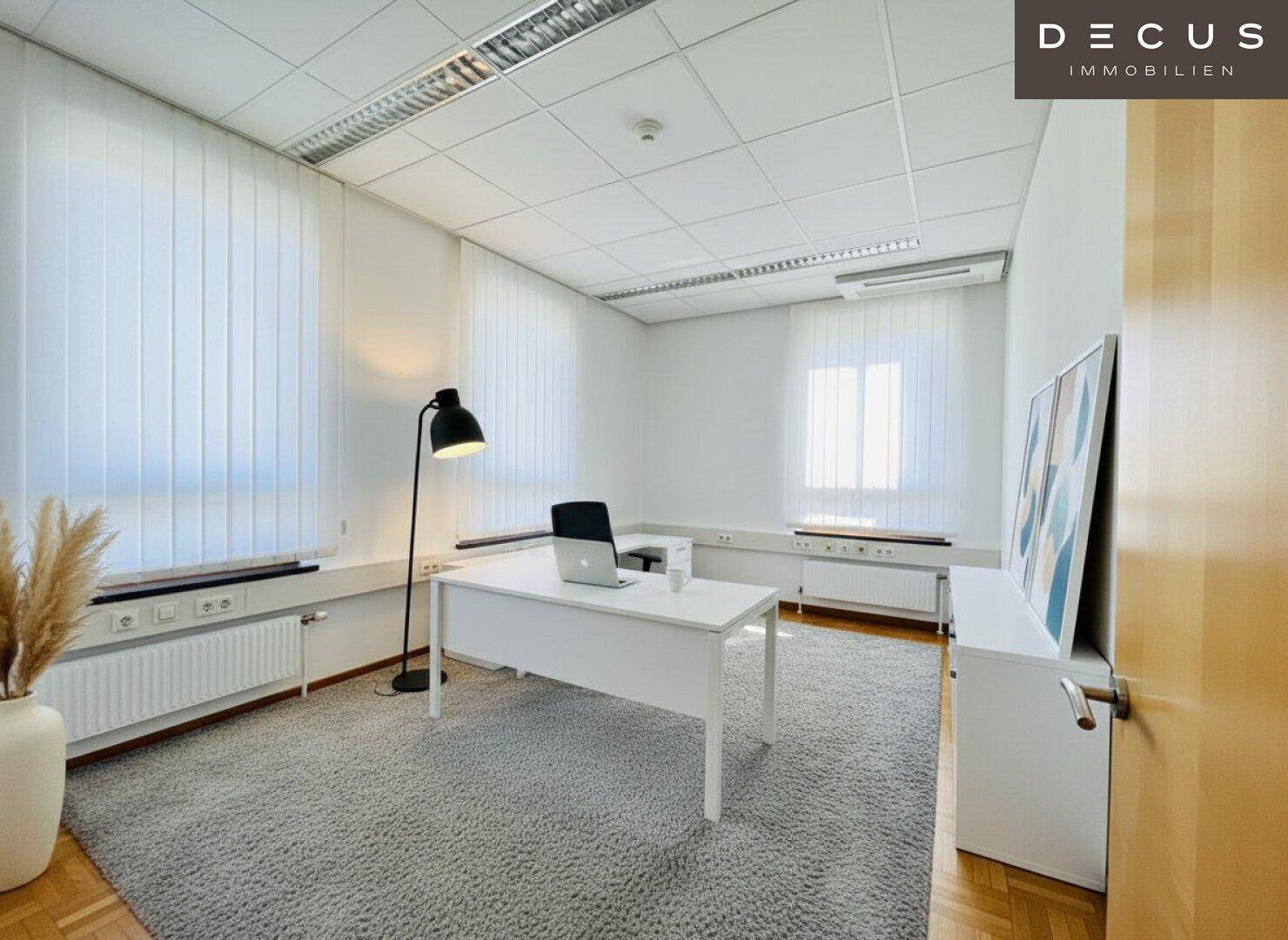 Einzelbüro mit weißem Schreibtisch, Teppichboden und großen Fenstern mit Jalousien für Privatsphäre.