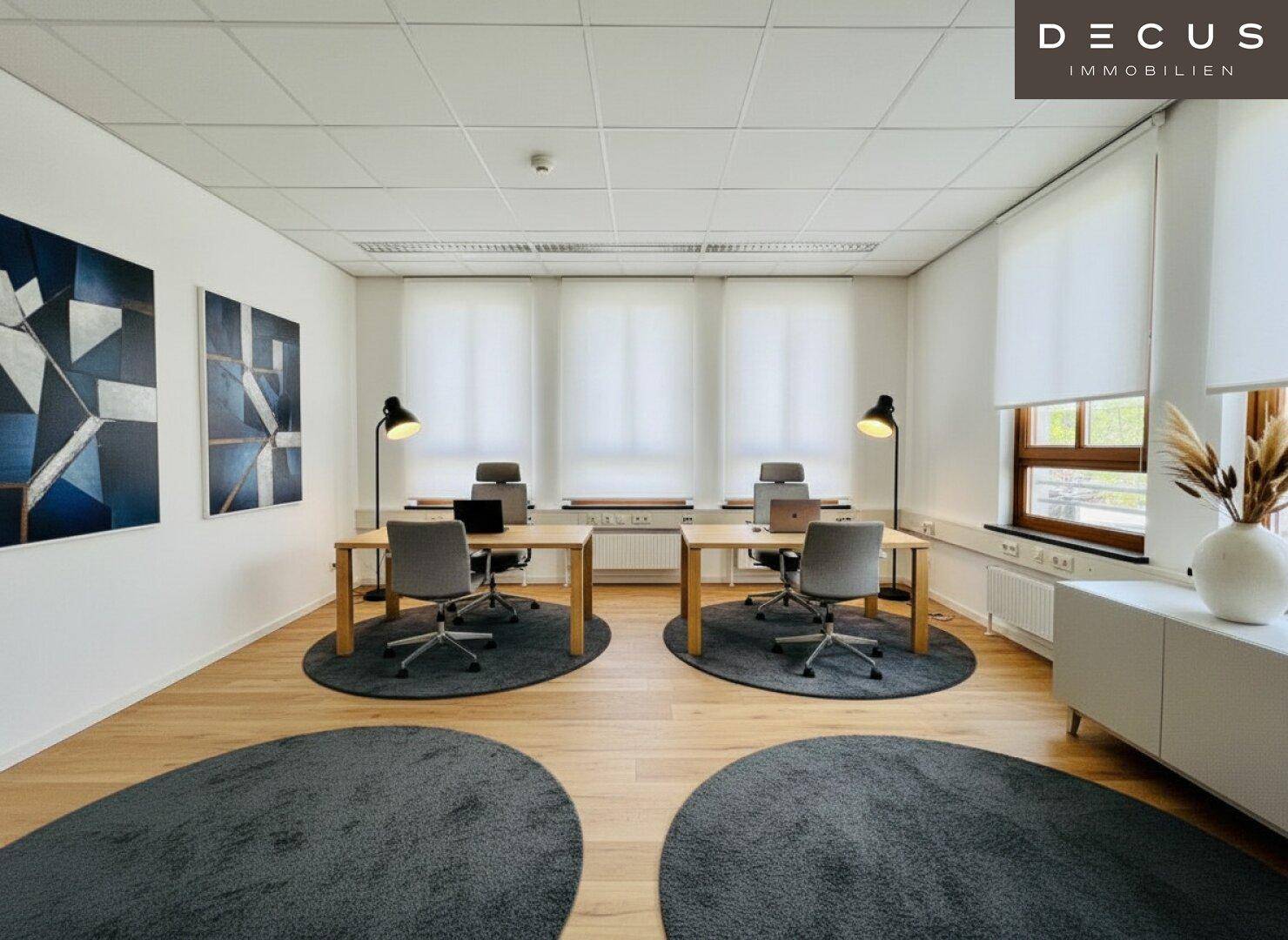 Helles Büro mit zwei Arbeitsplätzen, Holzboden und modernen Kunstwerken an den Wänden.