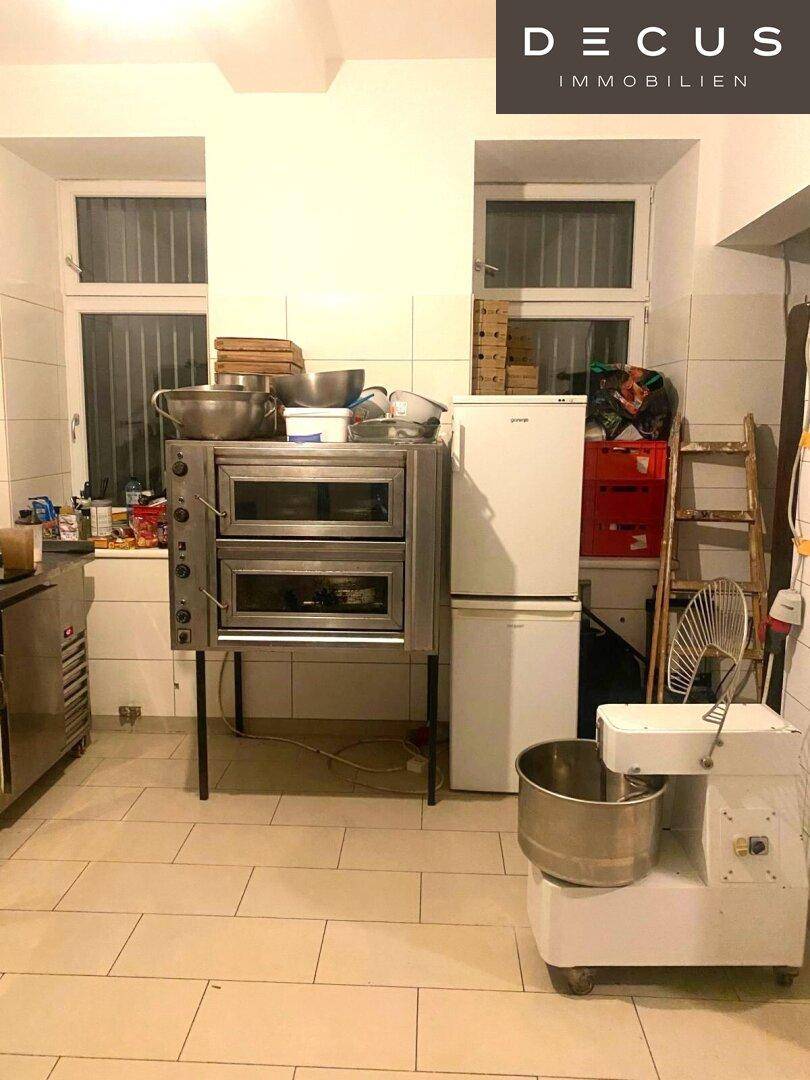 Geräumige Gewerbeküche mit Backöfen, Kühlschrank und großem Mixer, funktional eingerichtet.