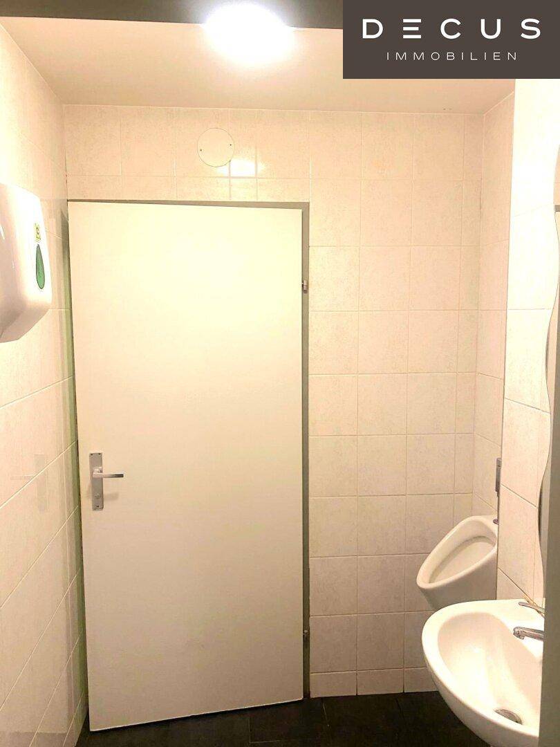 Gefliestes Badezimmer mit Urinal und Waschbecken, ausgestattet für den öffentlichen Gebrauch.