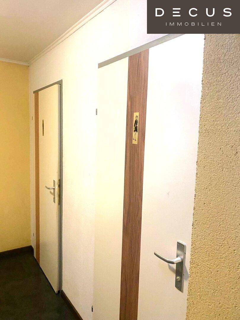 Schmaler Flur mit zwei Türen, eine davon mit einem Piktogramm versehen, sauber und funktional.