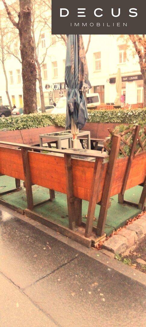 Außenbereich mit Holzbänken und Sonnenschirm, bereit für Gäste und Passanten.