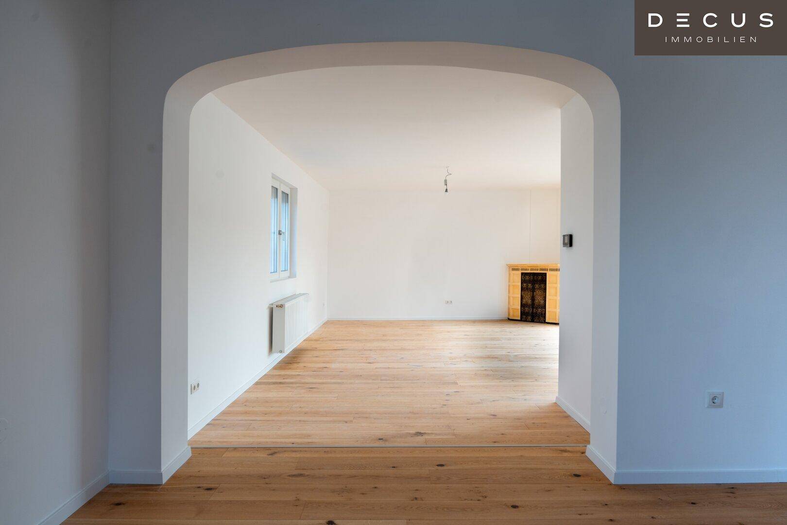 Heller Wohnbereich mit Holzboden und einem eleganten Rundbogen, der Räume stilvoll verbindet.