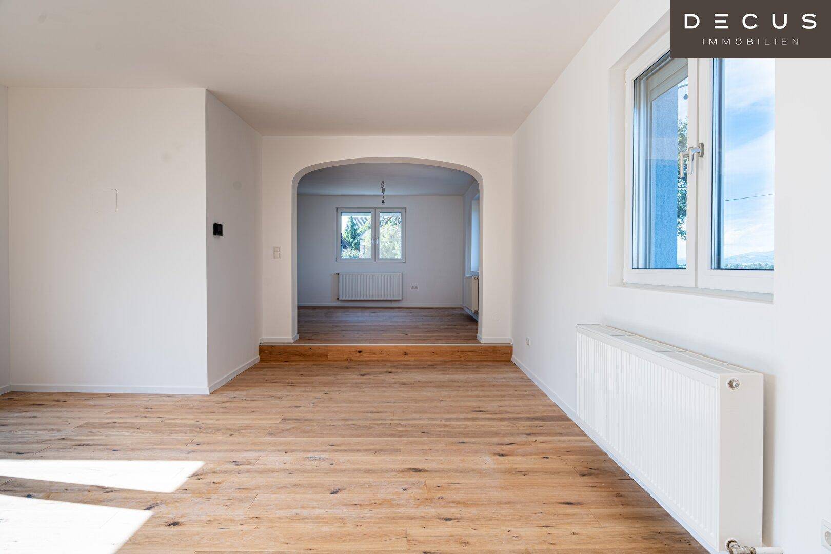 Heller Raum mit Holzboden, Heizkörper und einem Rundbogen, der zu einem weiteren Bereich führt.
