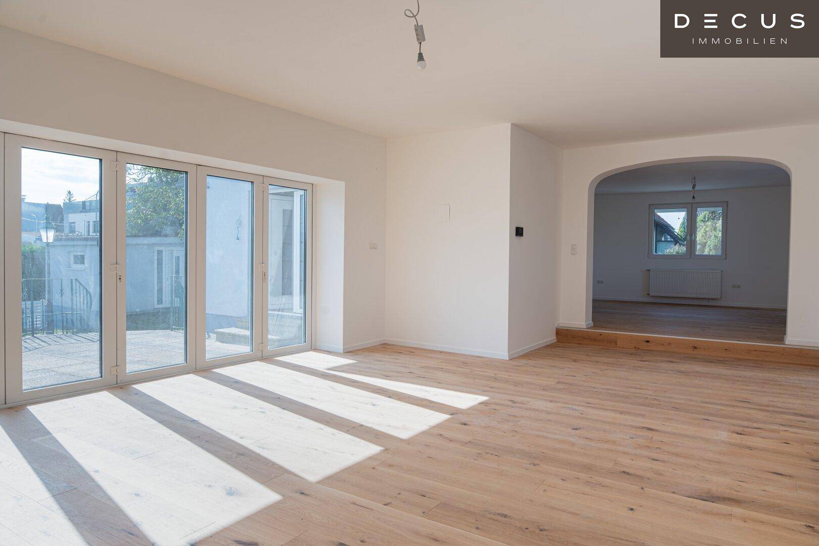 Lichtdurchfluteter Raum mit Holzboden und großen Fenstertüren, die zum Garten führen.