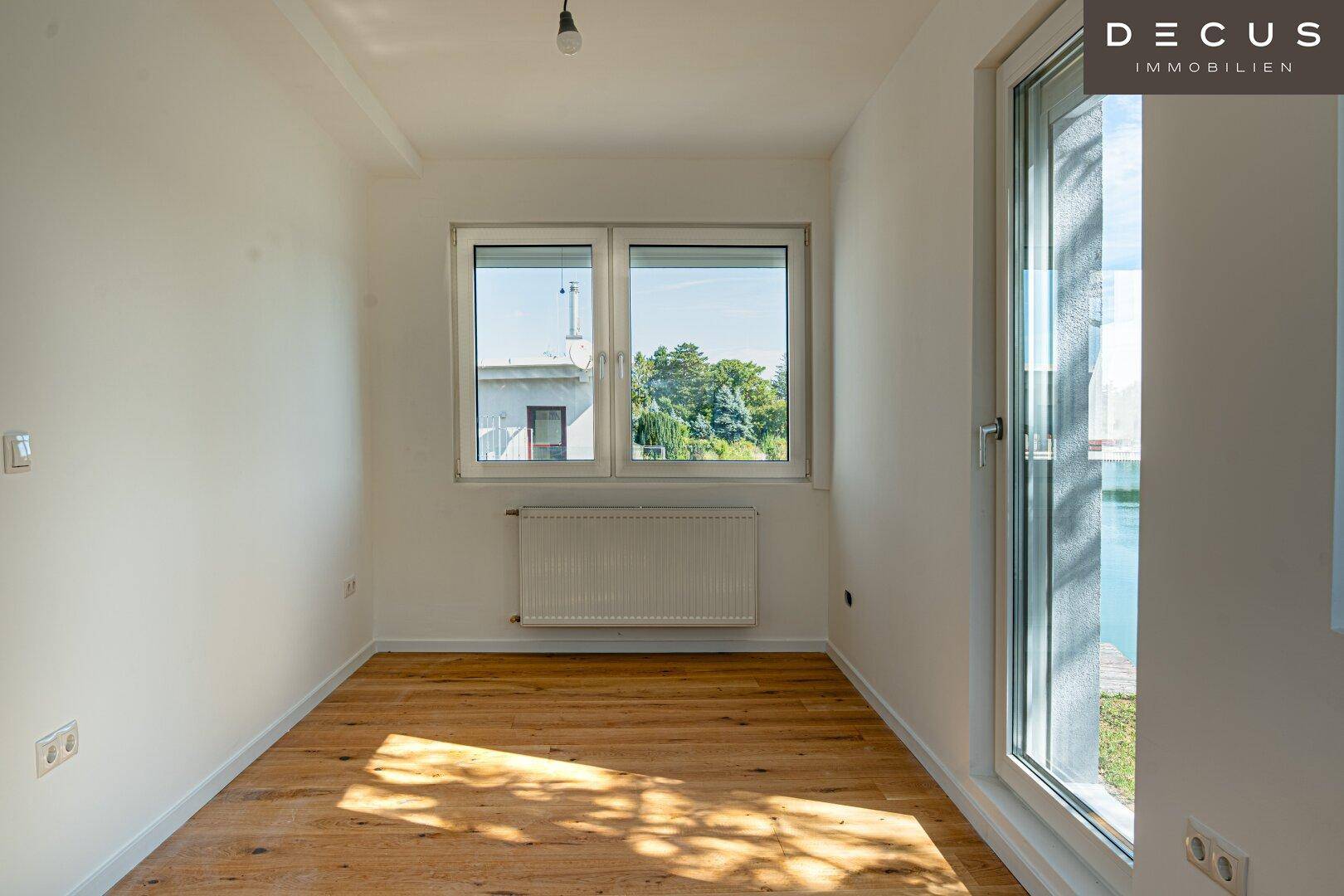 Leerer Raum mit Holzboden und Fenster mit Blick auf den See, ideal für ein Schlafzimmer.