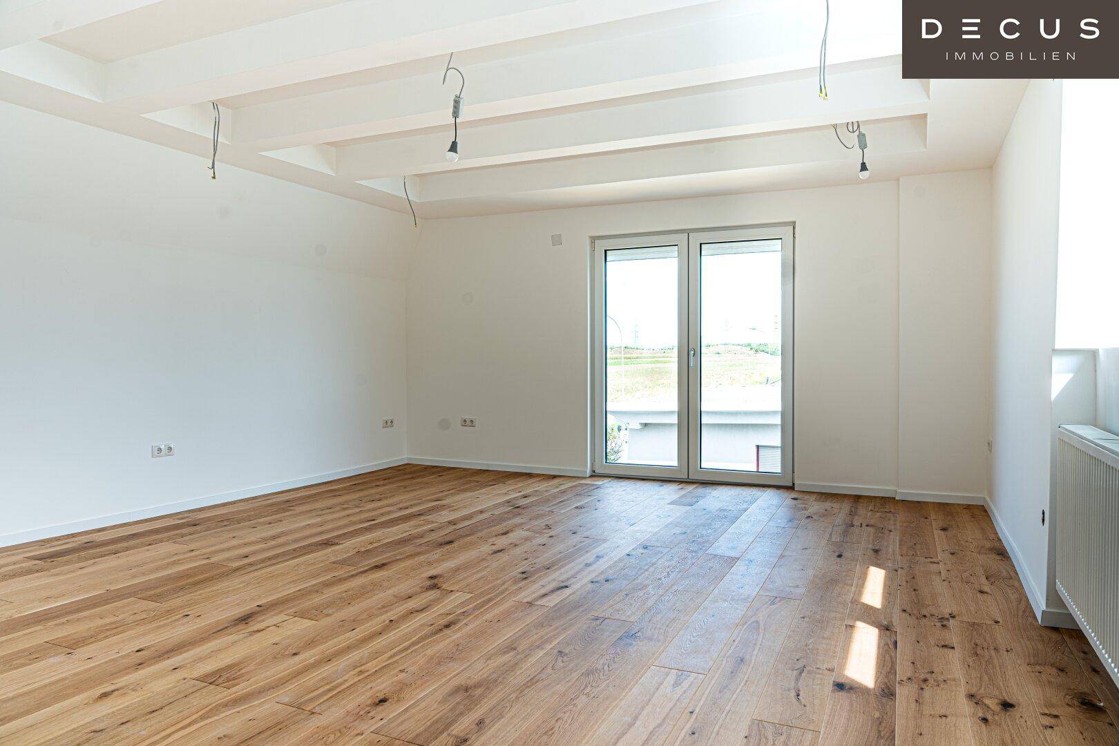 Geräumiger leerer Raum mit Holzboden und großen Fenstertüren, die ins Freie führen.