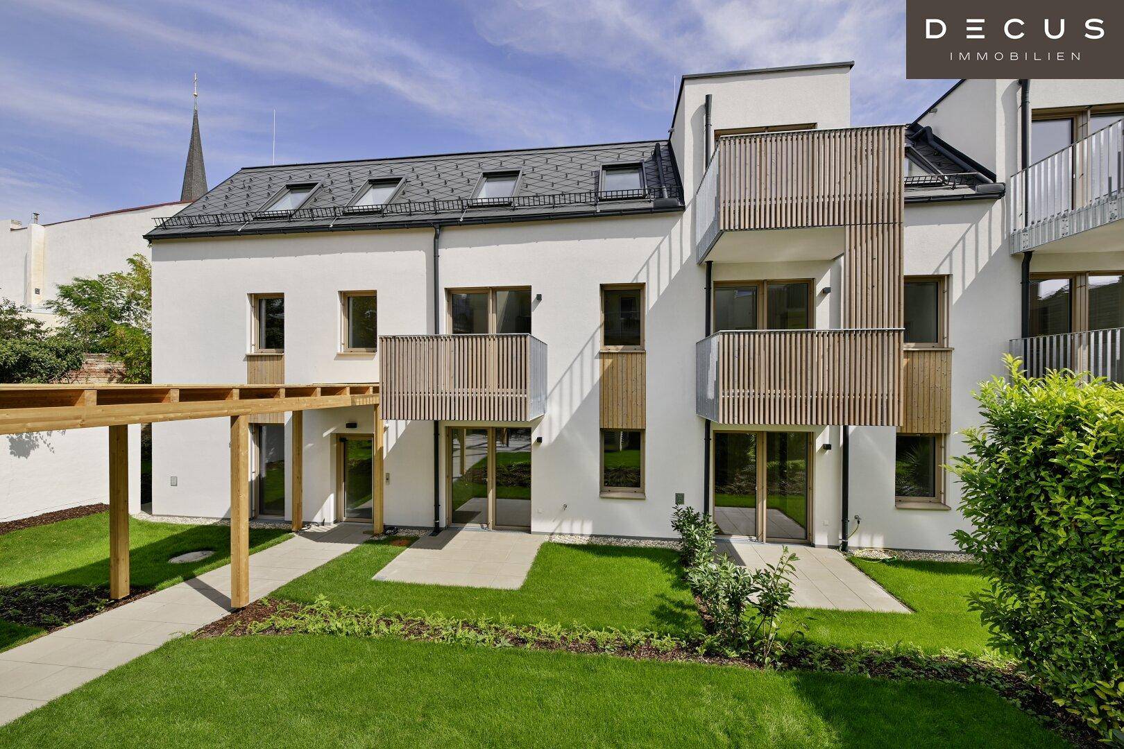 Attraktive Neubau-Fassade mit Holzpergola, gepflegtem Rasen und Balkonen im Sonnenlicht.