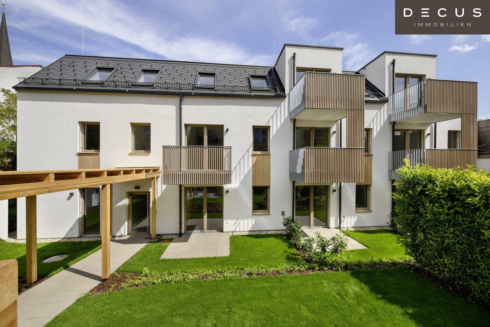 Moderne Wohnanlage mit heller Fassade, Holzdetails und grüner Gartenanlage.