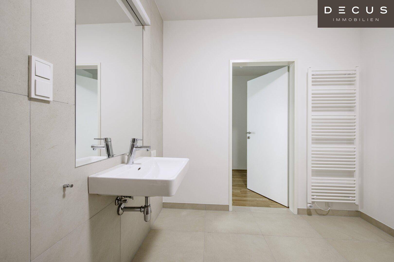 Modernes Badezimmer mit hellem Fliesenboden, Waschbecken und praktischem Handtuchheizkörper.