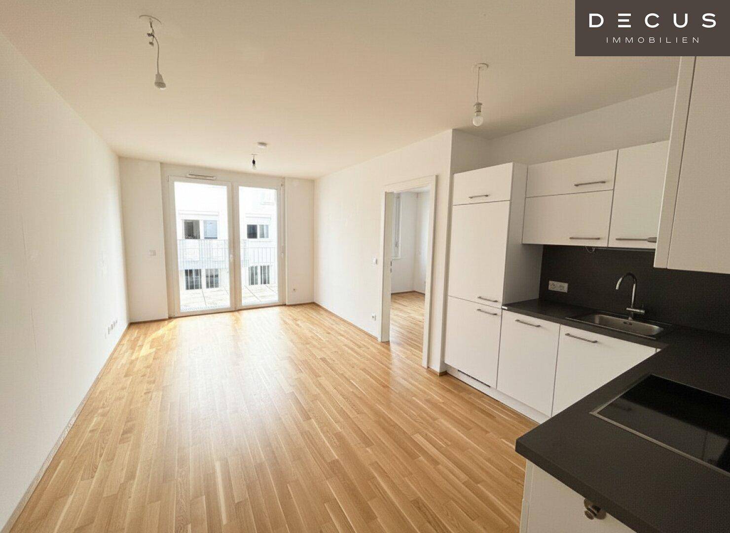 Offener Wohnbereich mit integrierter Küchenzeile, Parkettboden und Zugang zum Balkon.