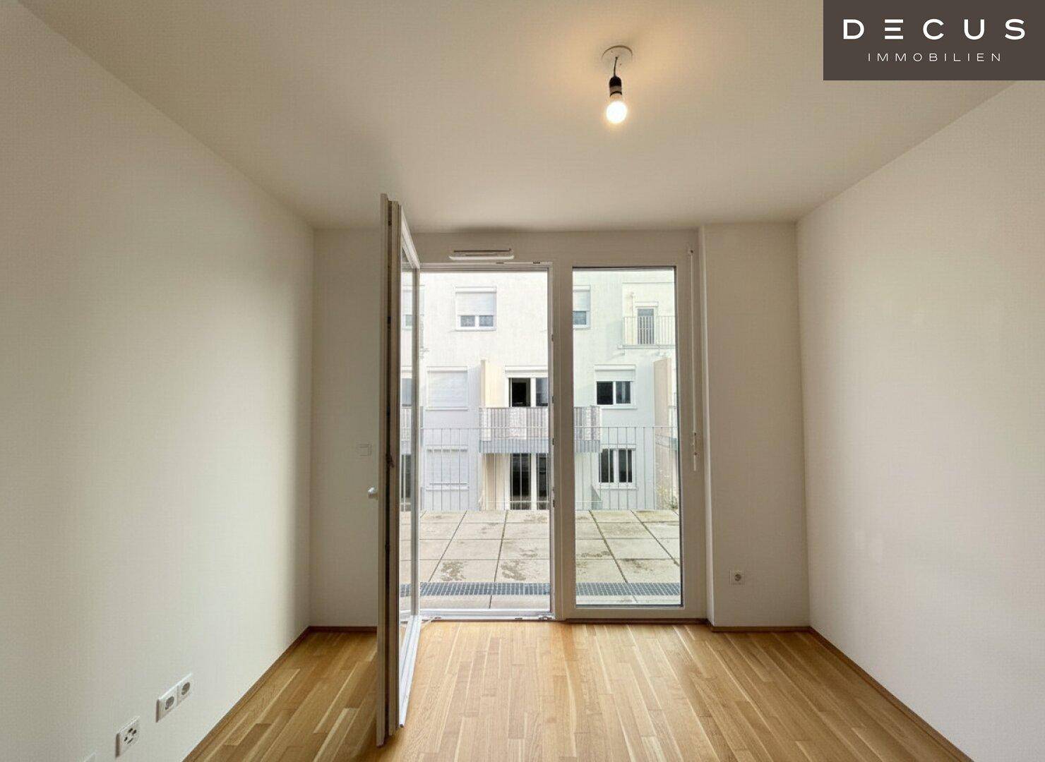 Geräumiges, helles Zimmer mit Holzboden und großen Fenstern zum Außenbereich.