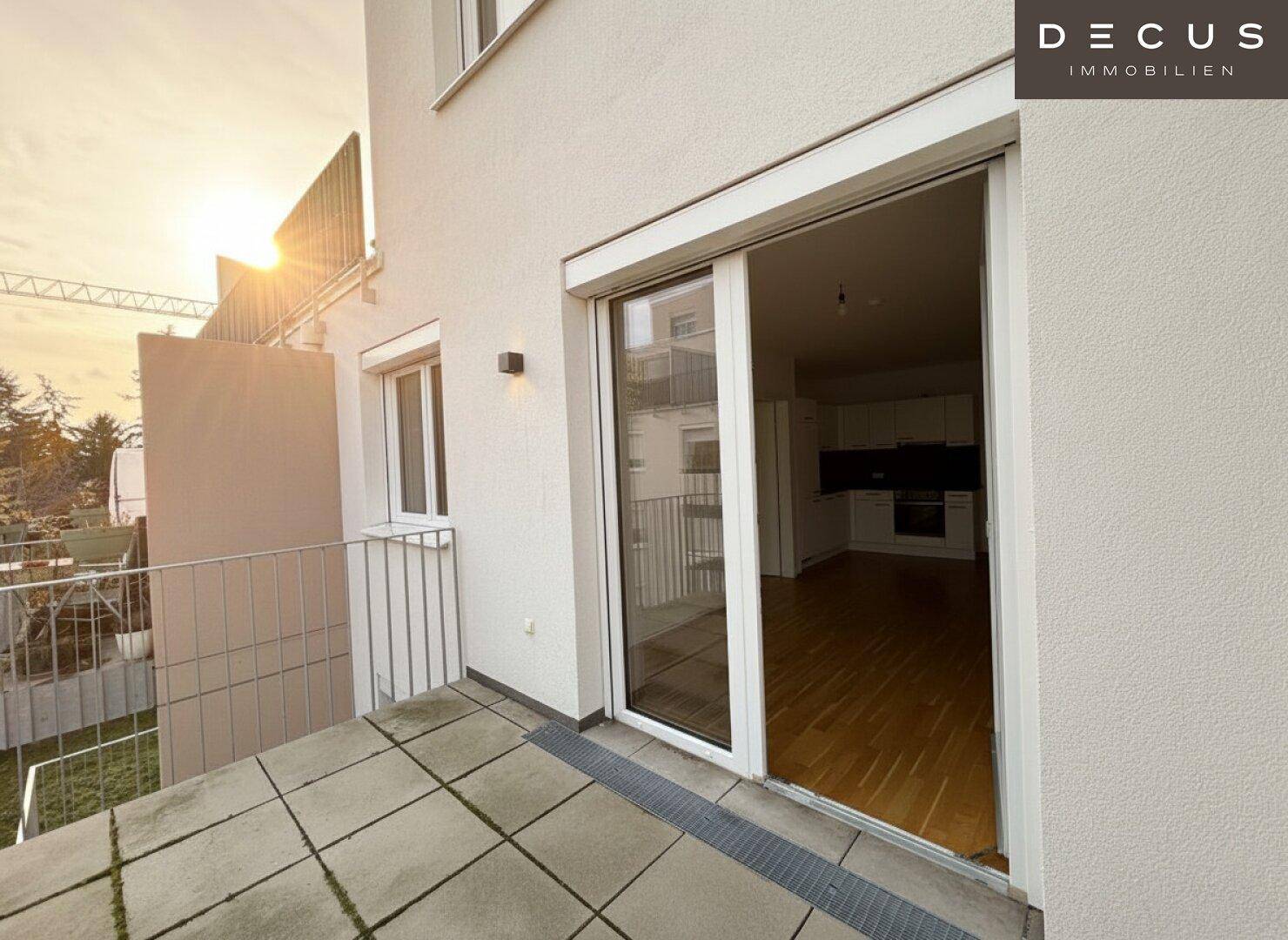 Sonniger Balkon mit Fliesenboden und Blick in die offene Wohnküche des Apartments.