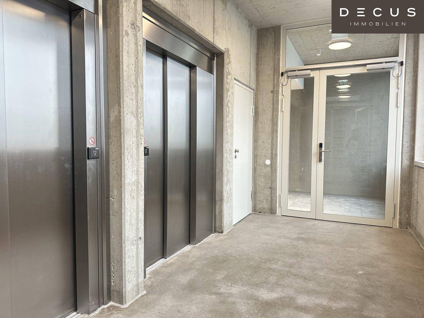 Moderner Aufzugsbereich mit zwei Aufzügen, Sichtbetonwänden und einem robusten Betonboden.