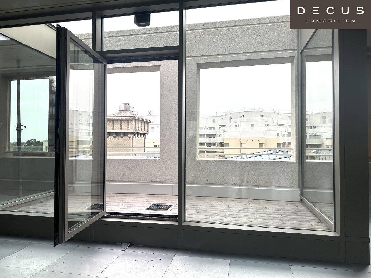 Innenraum mit großen Fenstern, die Zugang zu einem Balkon oder einer Terrasse bieten und Stadtblick.