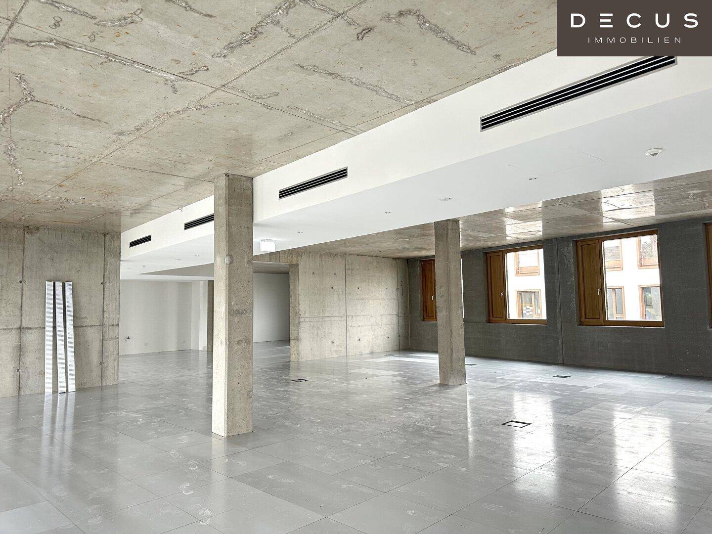 Heller Büroraum mit Sichtbetondecke, Säulen und modernen Lüftungsschlitzen, ideal für flexible Gestaltung.