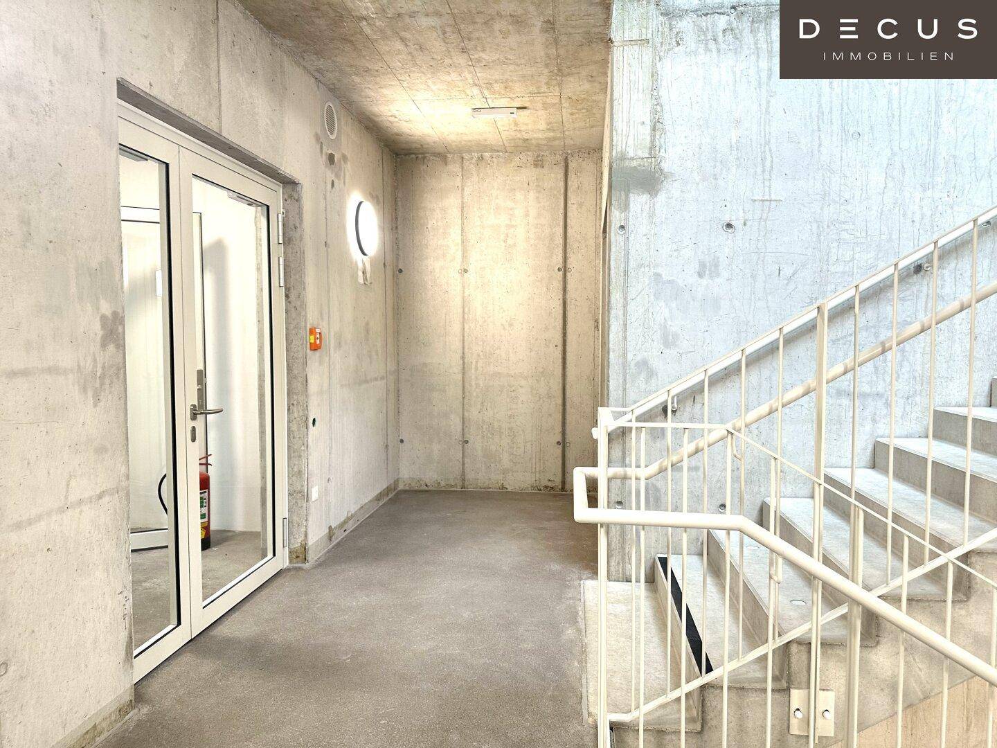 Treppenhaus mit Sichtbetonwänden und Metallgeländer, führt zu weiteren Etagen des Gebäudes.