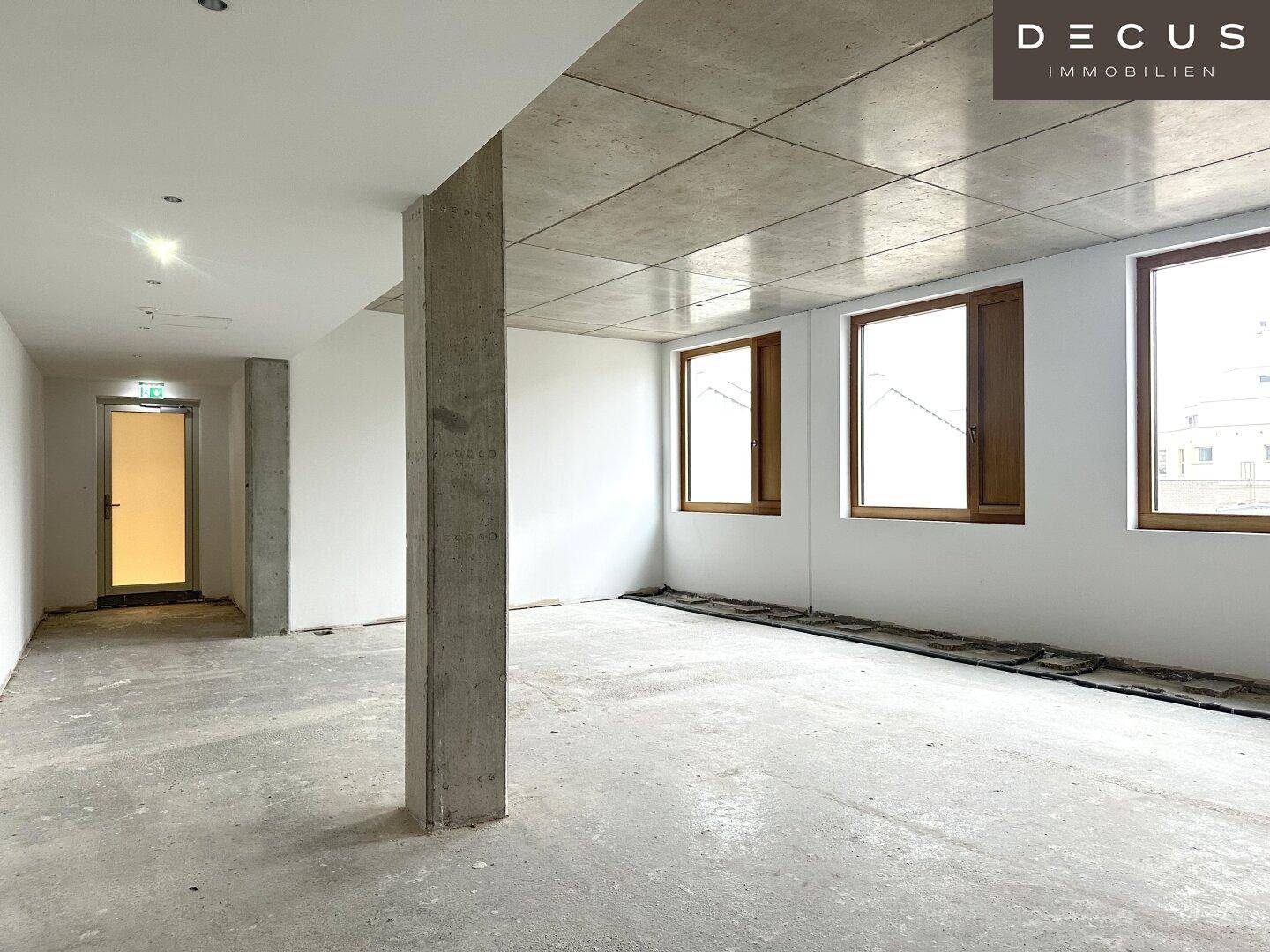 Geräumiger, unmöblierter Raum mit Betonboden, einer tragenden Säule und viel Tageslicht.