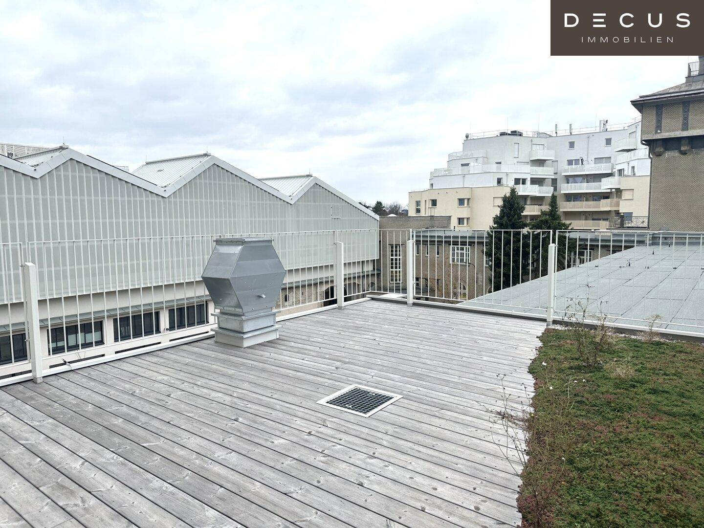 Große Dachterrasse mit Holzboden und Blick auf die umliegende moderne Architektur und Dächer.