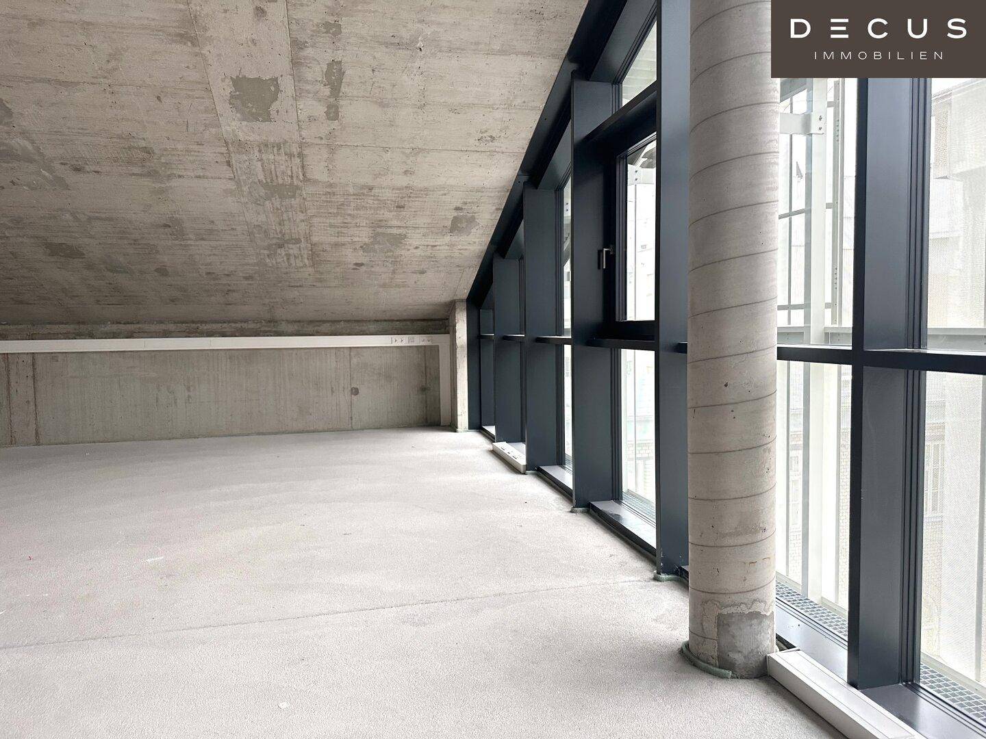 Geräumiger Innenraum mit Sichtbeton, einem Betonpfeiler und großen, schrägen Fensterfronten.