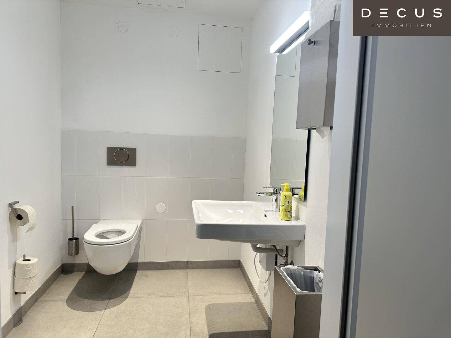 Modernes Badezimmer mit wandhängender Toilette, Waschbecken und Spiegel, ausgestattet mit hellen Fliesen.