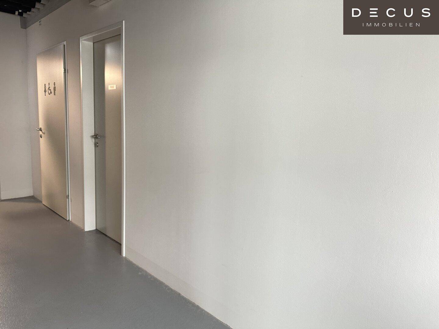 Heller Flur mit mehreren Türen und grauen Böden in einem modernen Gebäude.