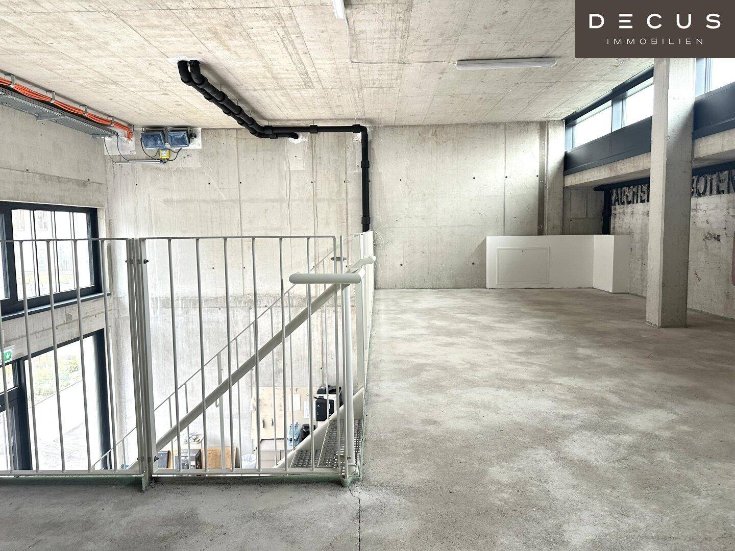 Geräumiger, unfertiger Obergeschossbereich mit Sichtbetonwänden und -decken sowie sichtbaren Installationen.