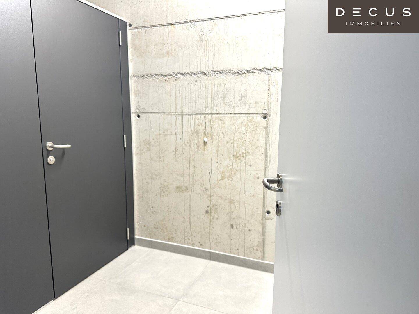Zwei Türen in unterschiedlichen Grautönen vor einer Betonwand mit Fliesenboden in einem unfertigen Bereich.