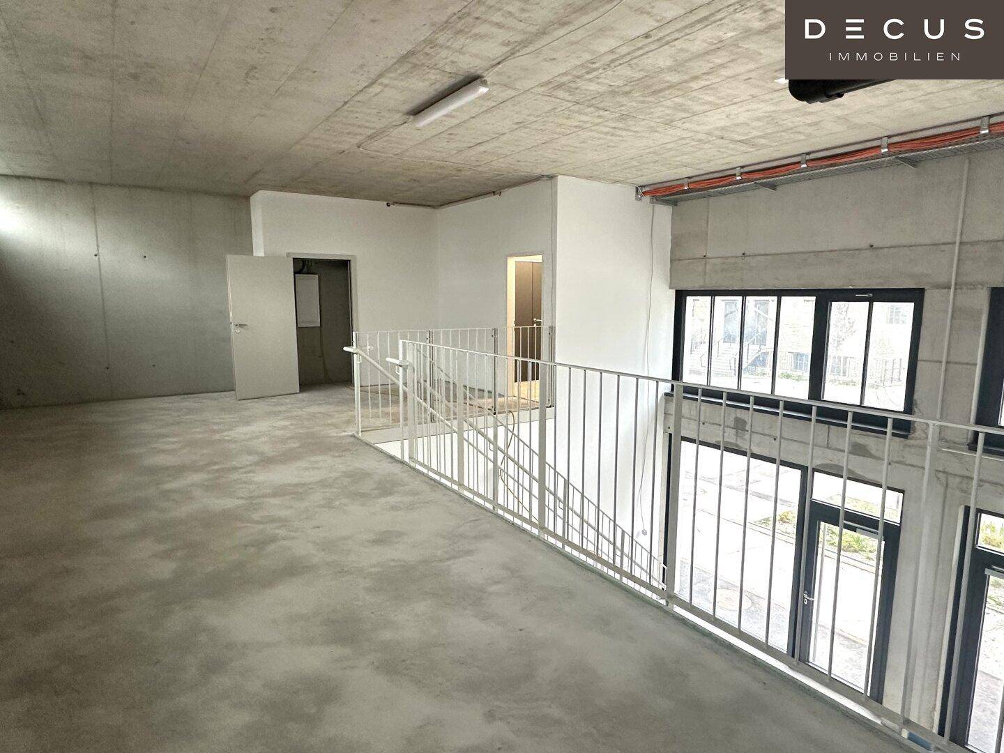 Großer, unfertiger Raum im Obergeschoss mit Betonoberflächen und großen Fenstern, die den Blick nach draußen ermöglichen.