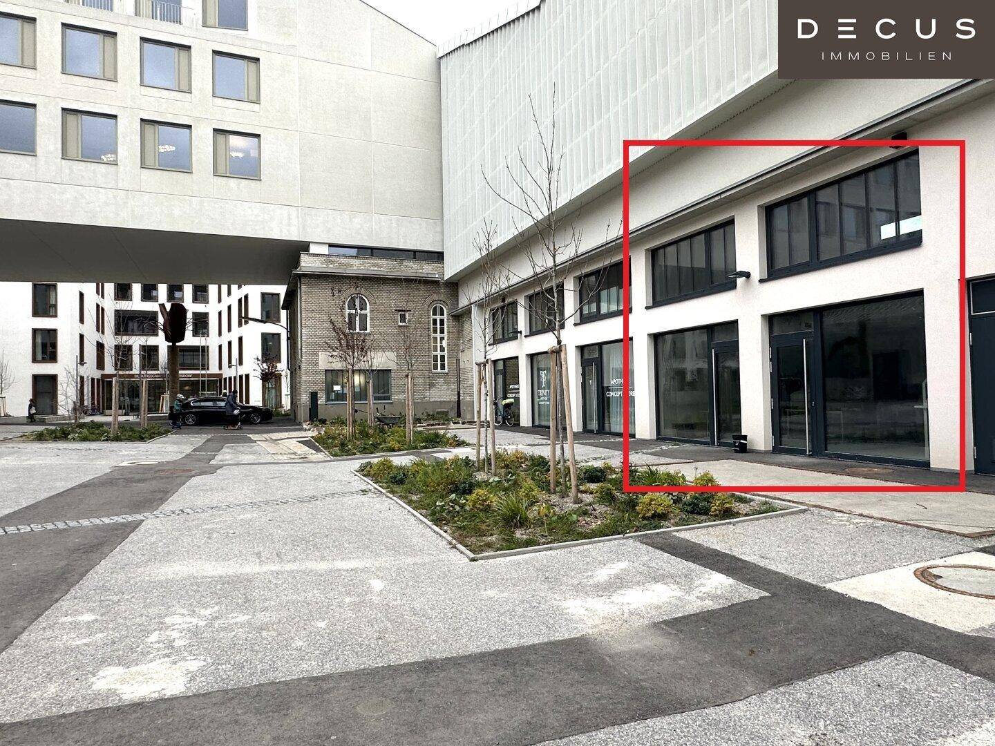 Außenansicht eines modernen Gebäudekomplexes mit gepflastertem Vorplatz und angrenzenden Strukturen.