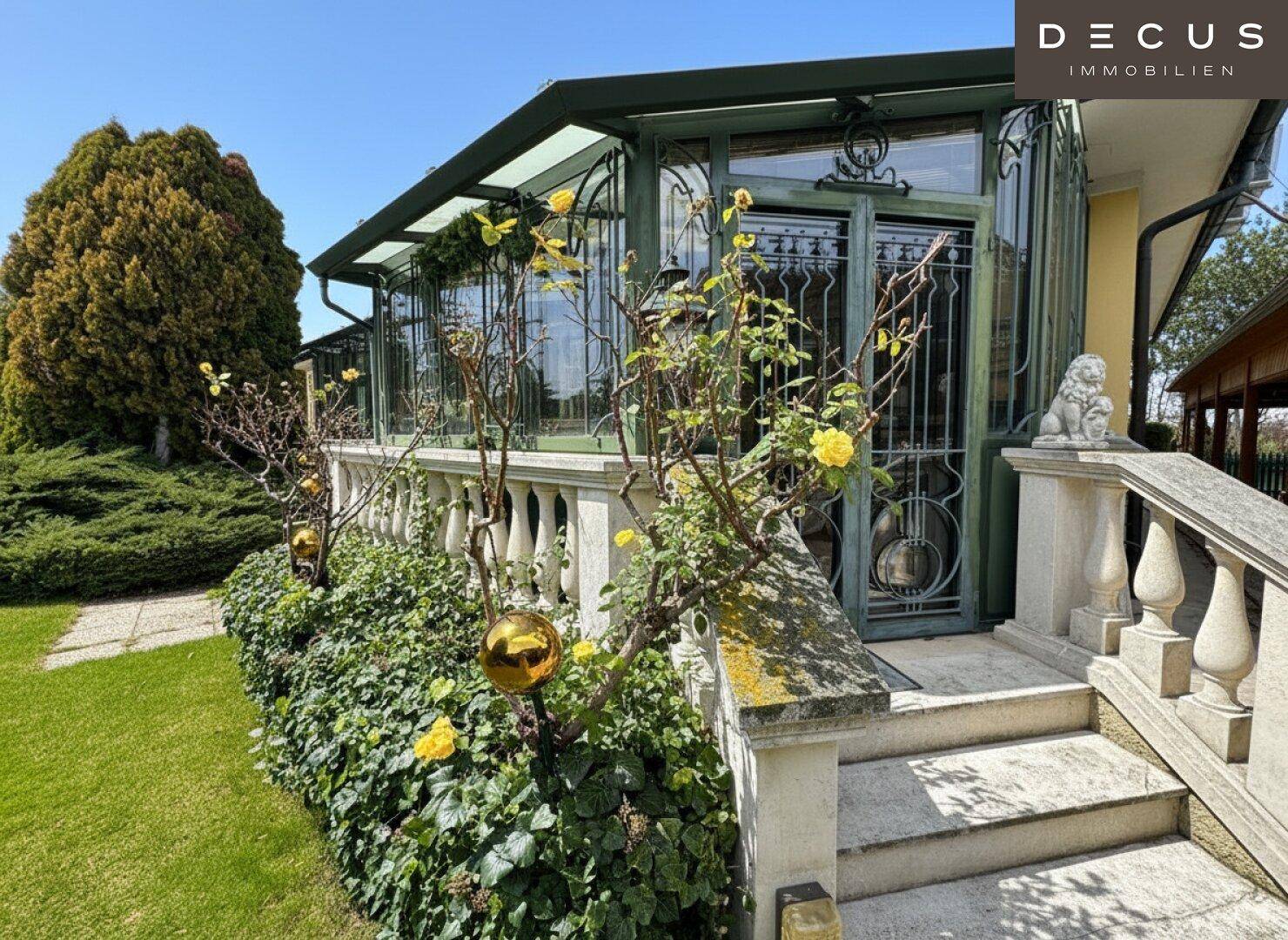 Eingangsbereich des Wintergartens mit blühenden Rosen, Steintreppe und gepflegtem Garten.