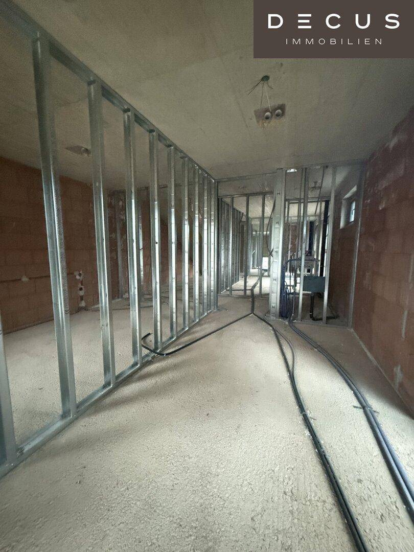Innenraum im Rohbau mit Metallständerwänden für die zukünftige Raumaufteilung und sichtbaren Ziegelwänden.