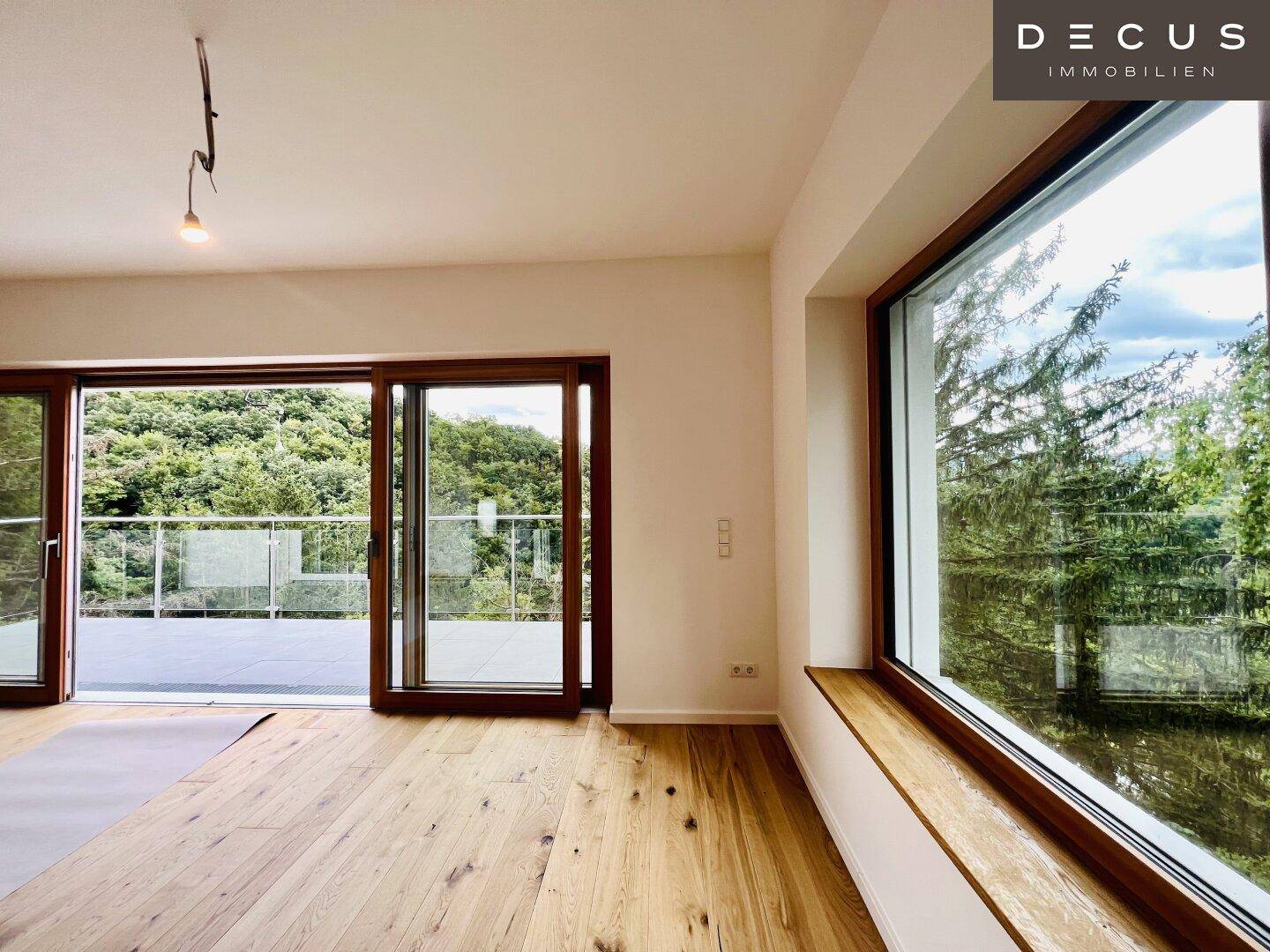Lichtdurchflutetes Wohnzimmer mit Holzboden, großen Fenstern und Zugang zum Balkon.