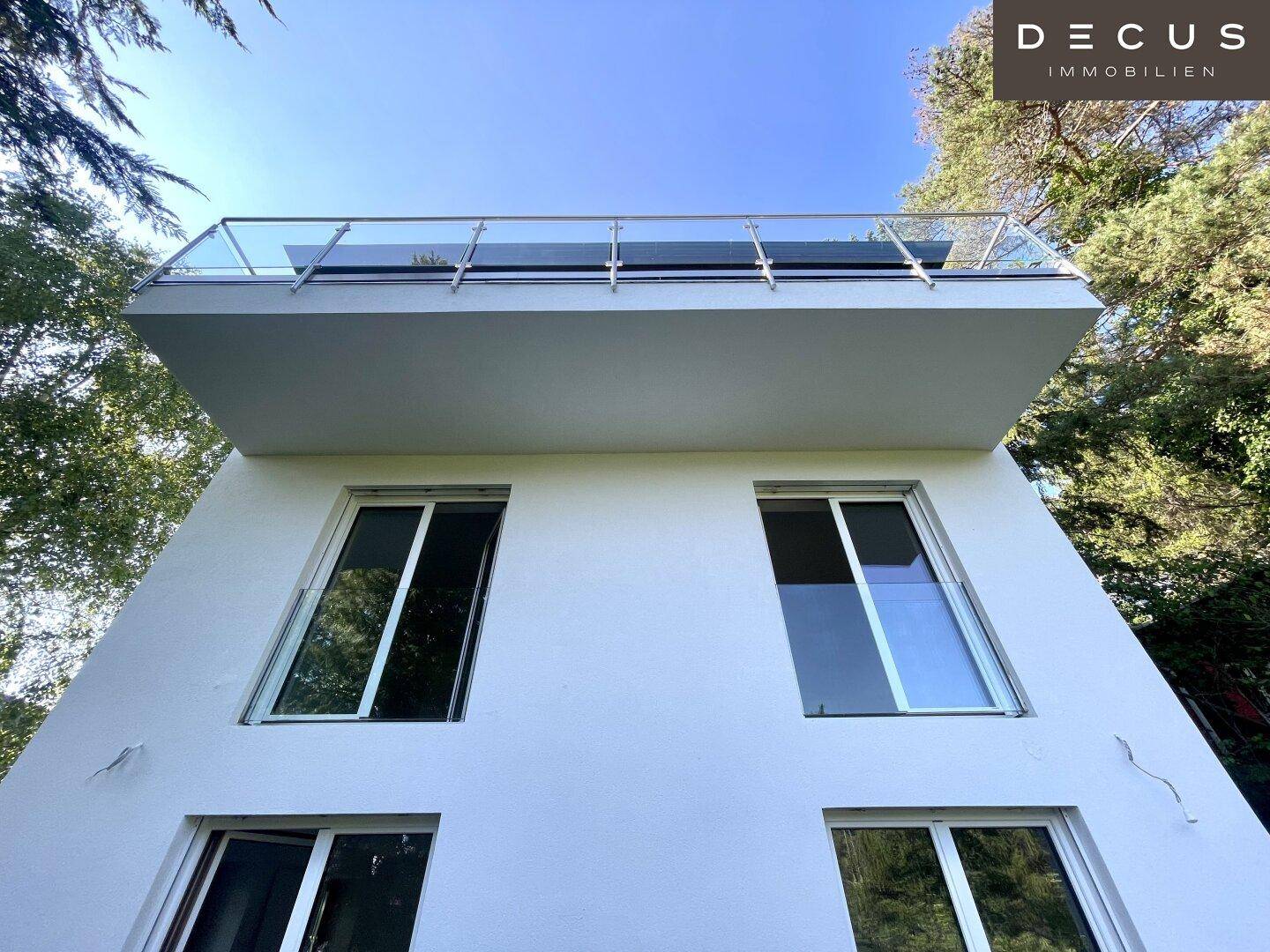 Moderne Architektur mit weißer Fassade und großem Balkon mit Glasgeländer.