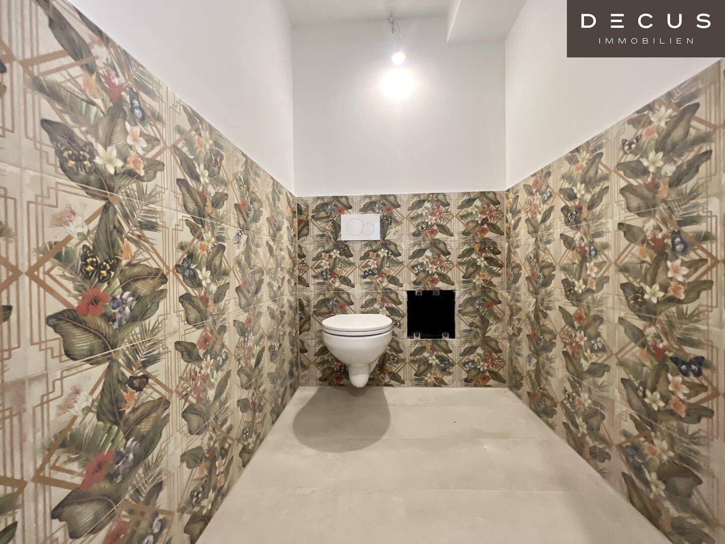Separate Toilette mit wandmontiertem WC und auffälligen, gemusterten Wandfliesen.