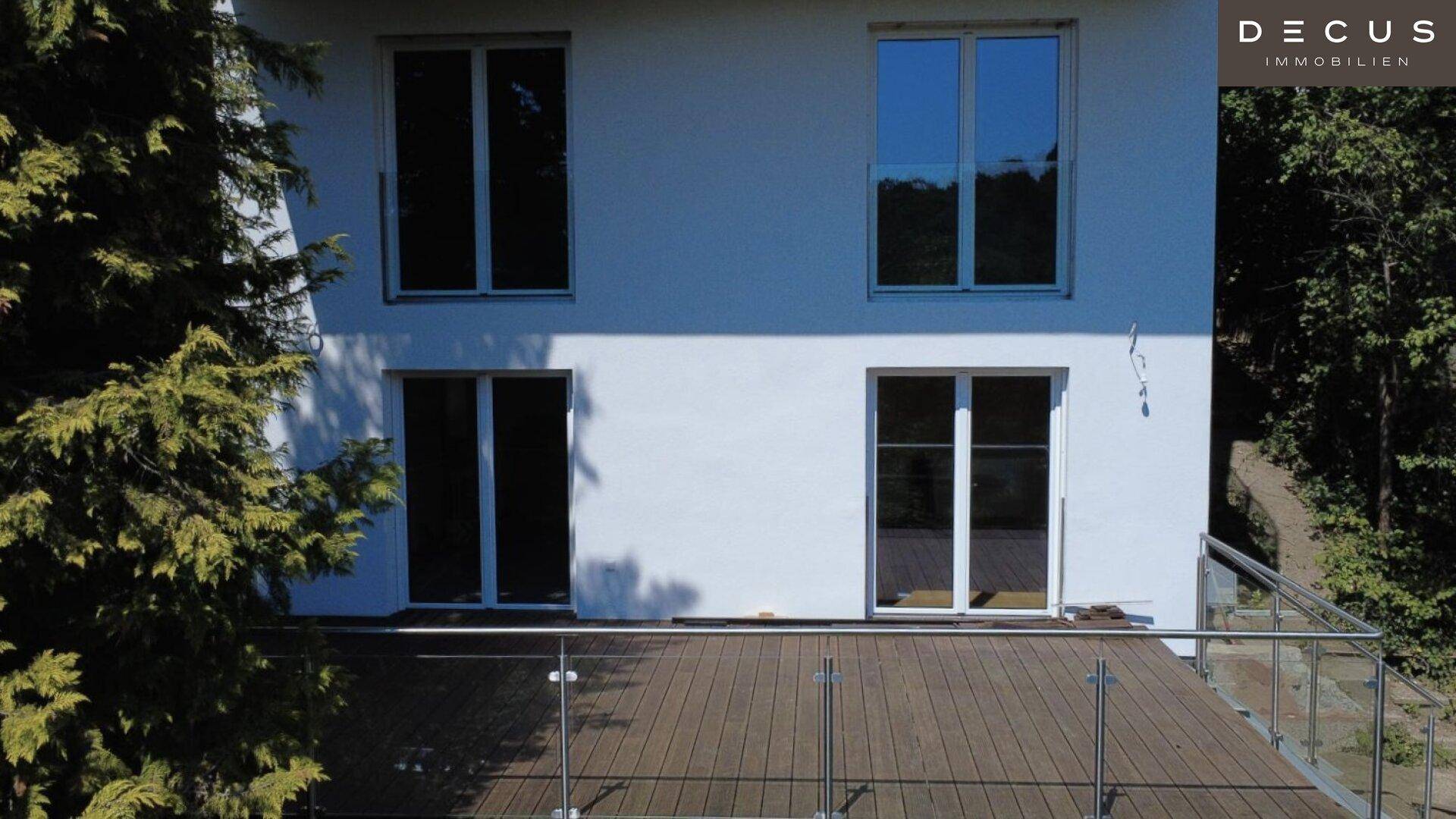 Unterer Bereich der Hausfassade mit großen Fenstern und Zugang zur Holzterrasse.