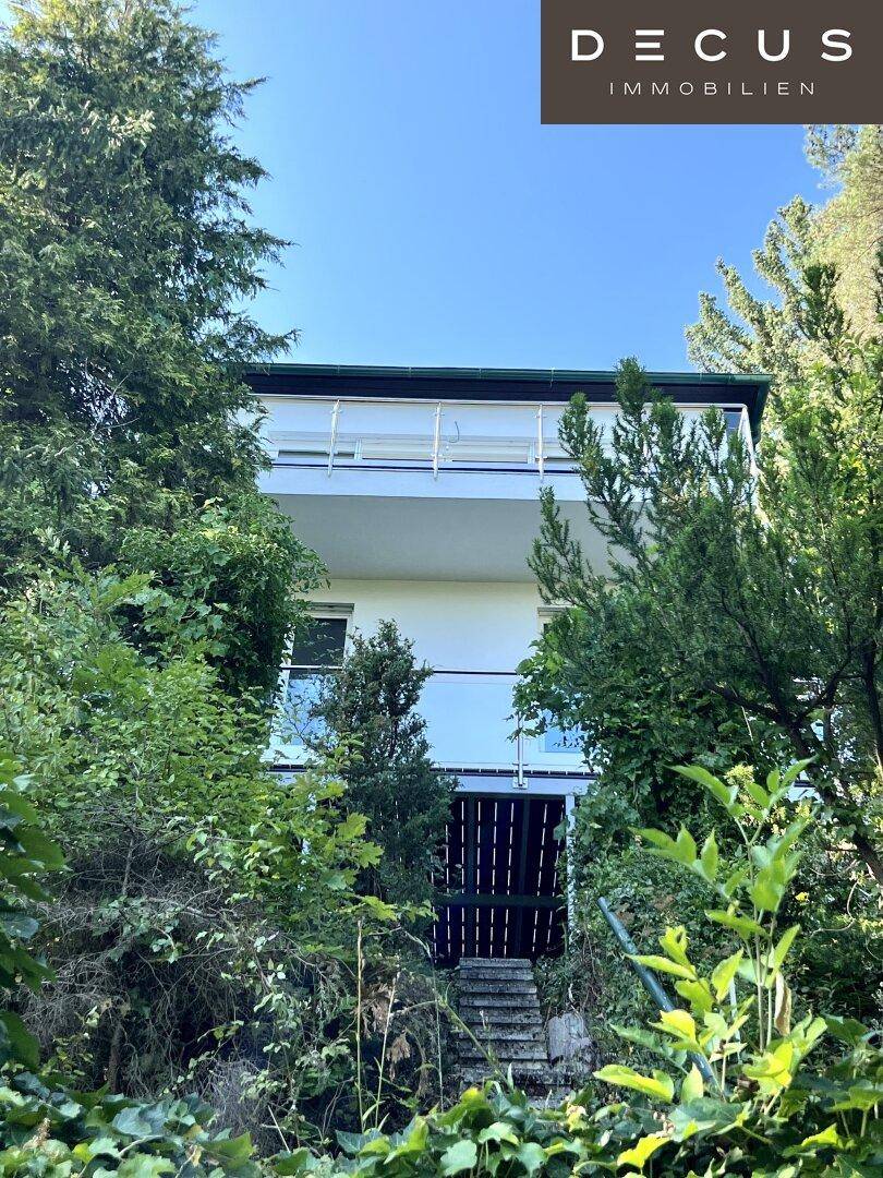 Hausfassade umgeben von üppiger Vegetation und Bäumen, mit Balkonen.