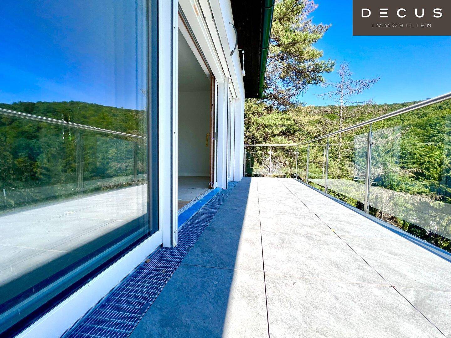 Sonniger Balkon mit Fliesenboden und Glasgeländer, bietet einen weiten Blick ins Grüne.