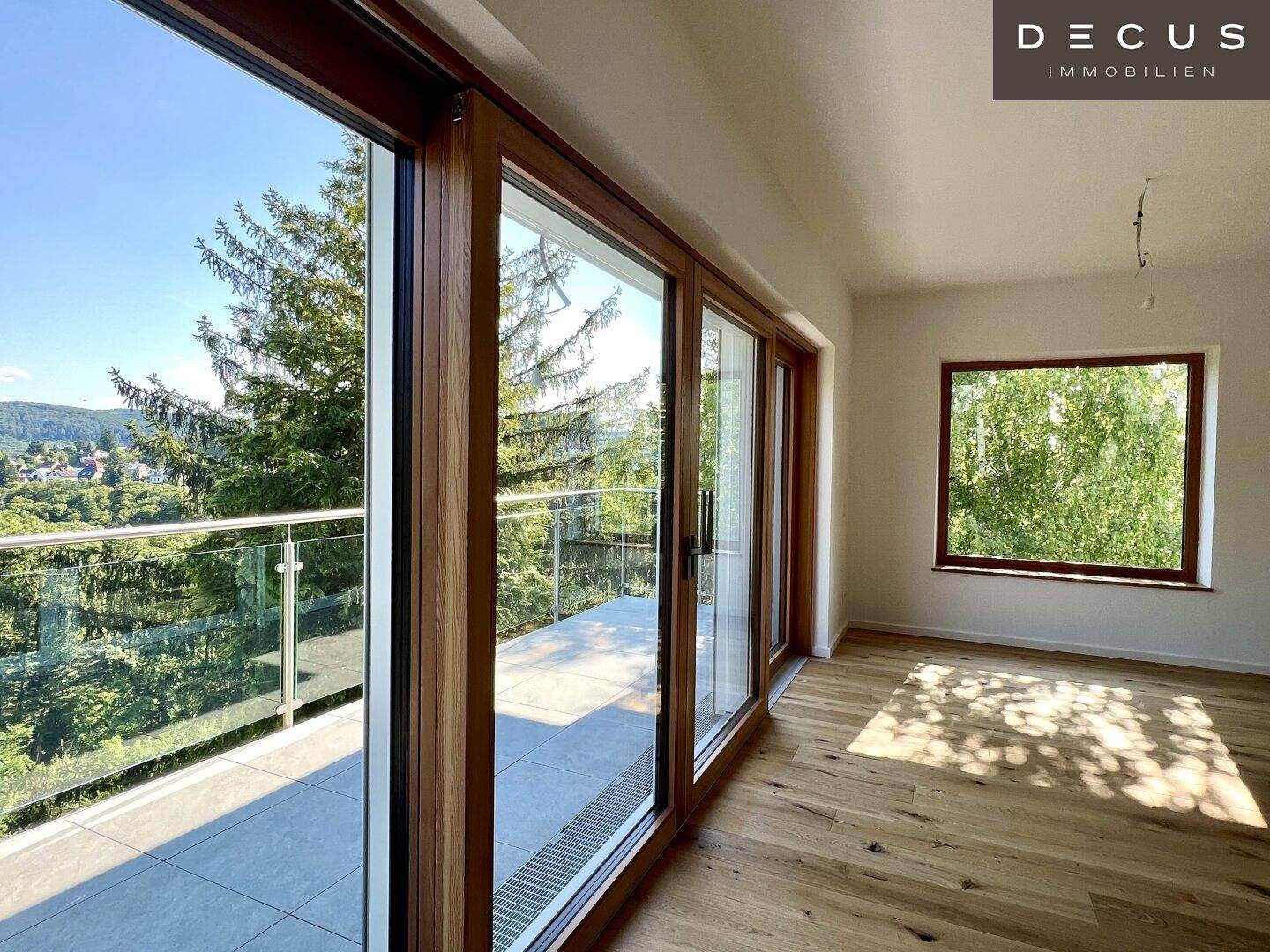 Lichtdurchfluteter Raum mit Holzboden und Zugang zu einem Balkon mit Panoramablick.