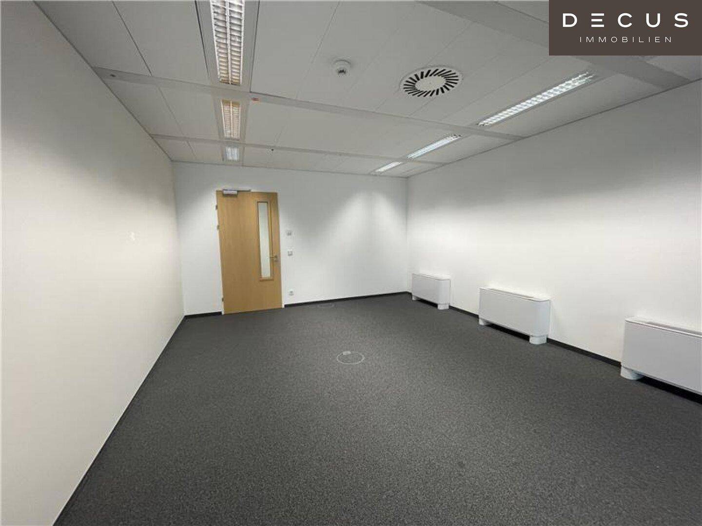 Leeres Büro mit Teppichboden und einer Holztür, bereit für die individuelle Einrichtung.