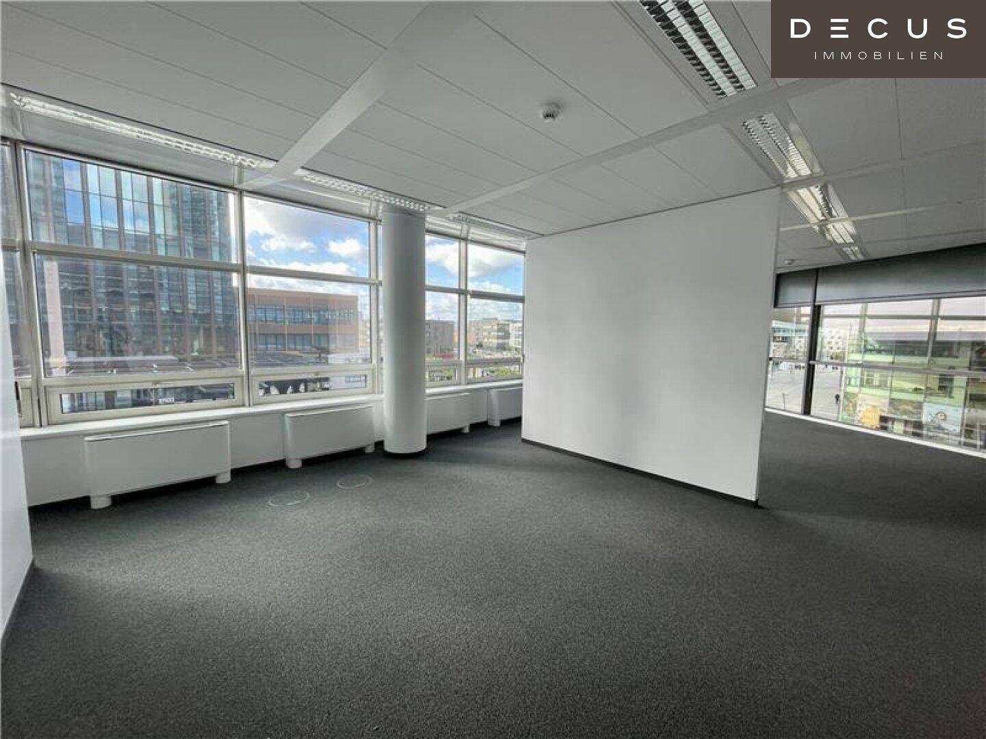 Geräumiges Büro mit Teppichboden und großen Fenstern, die viel Tageslicht hereinlassen.