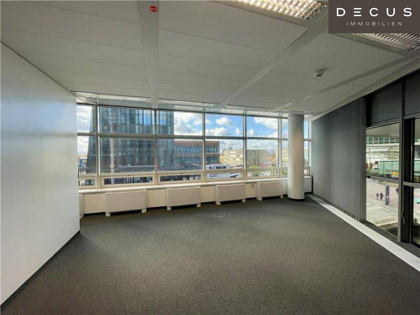Geräumiges Büro mit Teppichboden und großen Fenstern, die einen weiten Stadtblick ermöglichen.