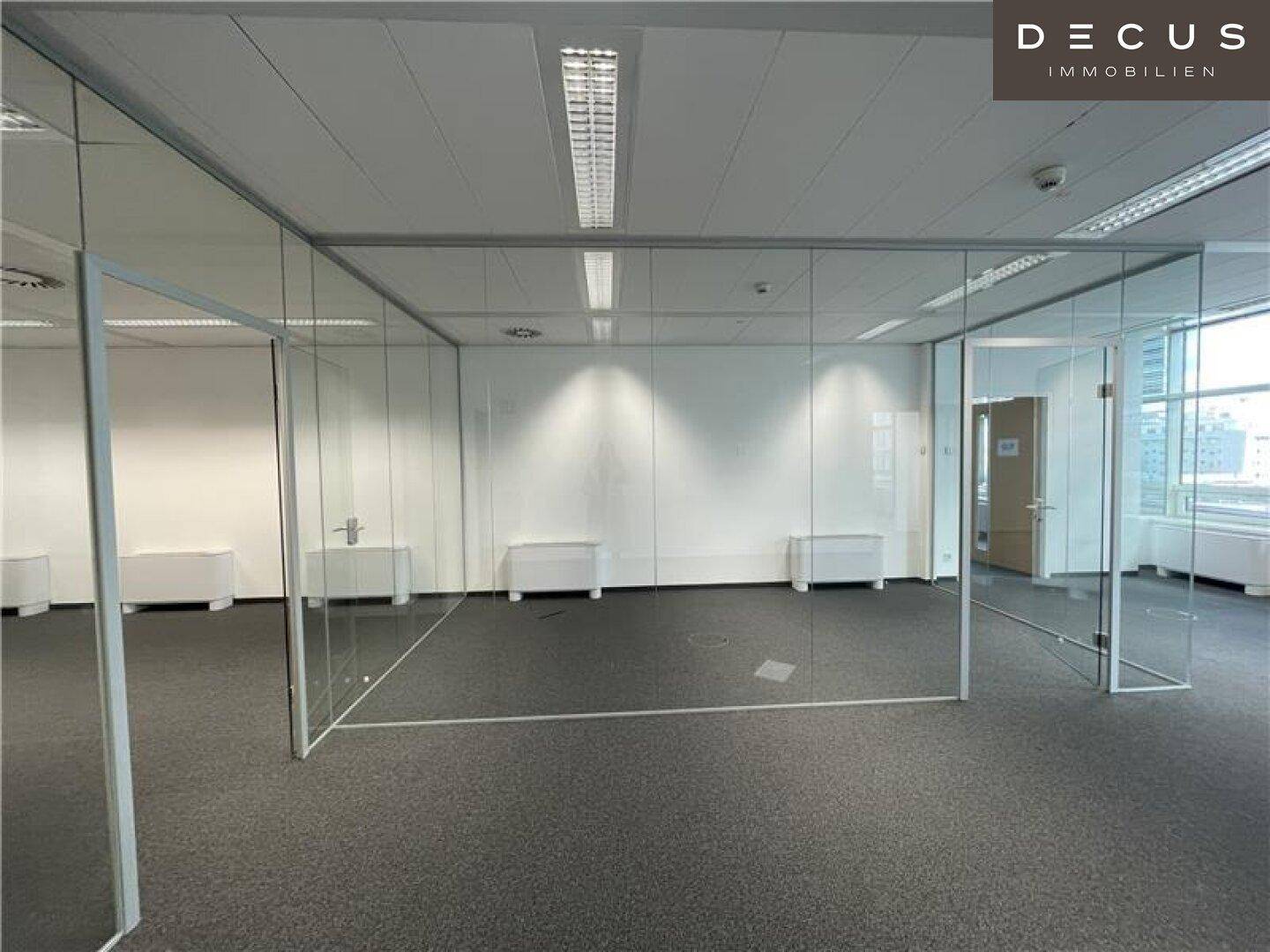 Großes Büro mit Teppichboden und Glaswänden, die flexible Raumaufteilung ermöglichen.
