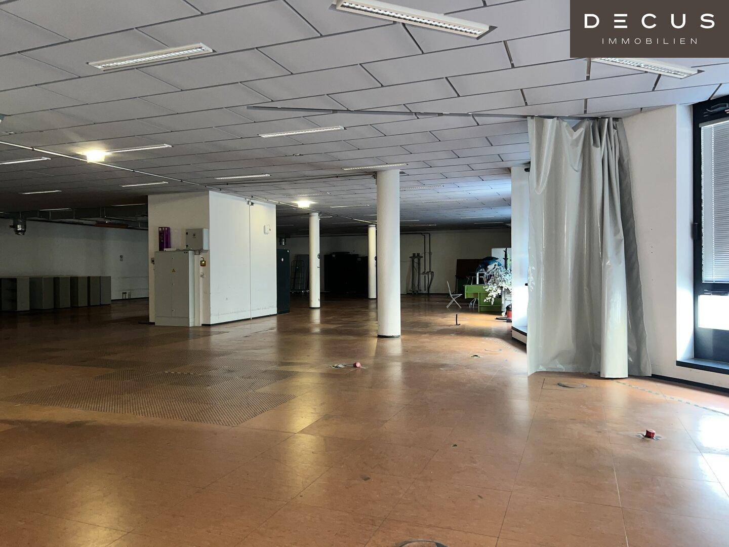 Weitläufiger Bürobereich mit Säulen, modularen Deckenplatten und großen Fenstern.